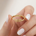 Solid gold criss cross ring held between fingers