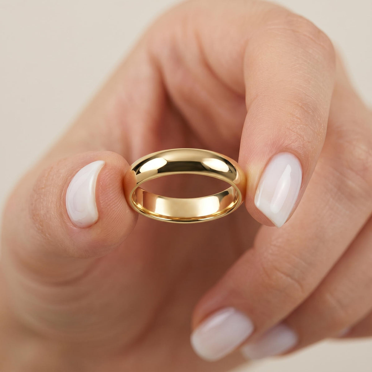 Solid gold 4mm dome wedding band held between fingers