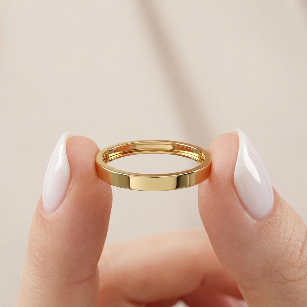 Solid gold 2mm flat wedding band held between fingers