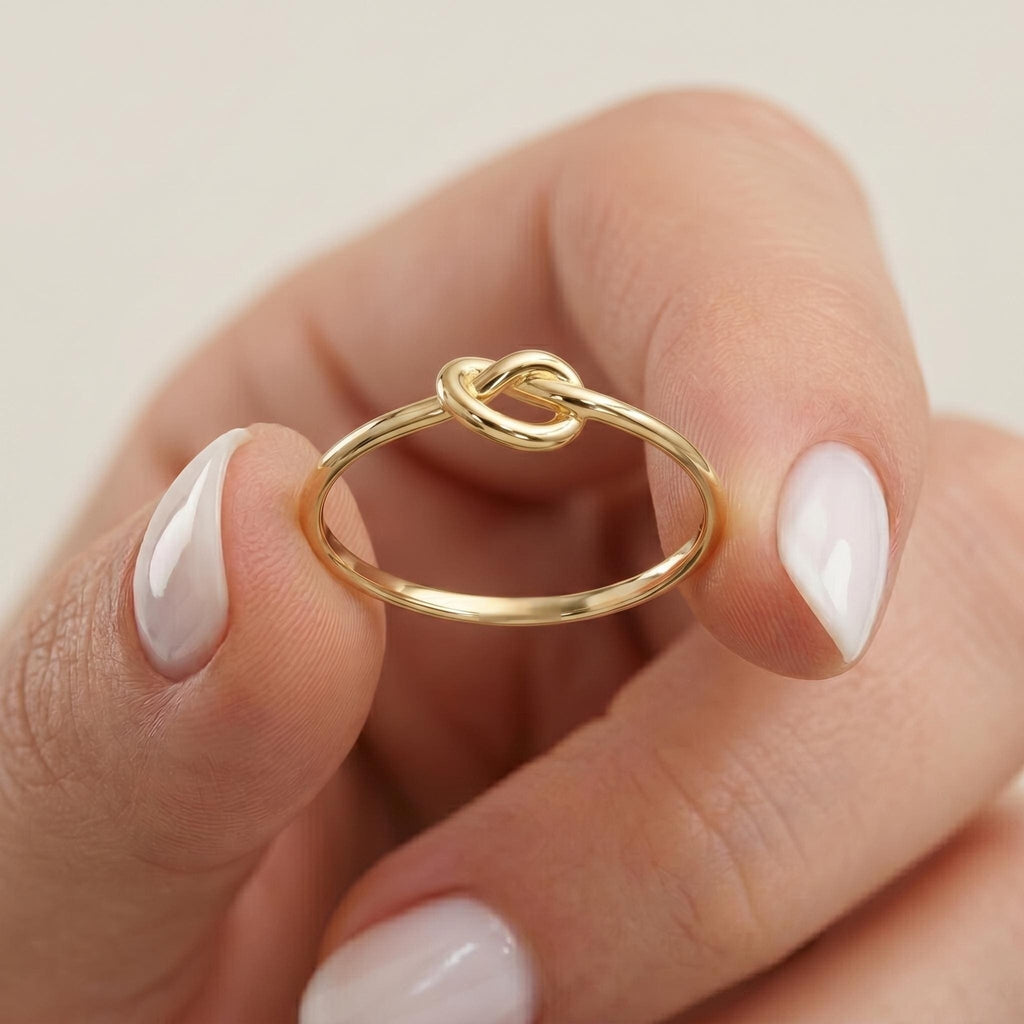 Love knot ring in 14k yellow gold held between two fingers