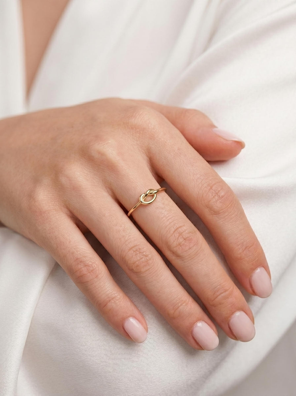 Thin gold love knot ring stacked on the finger