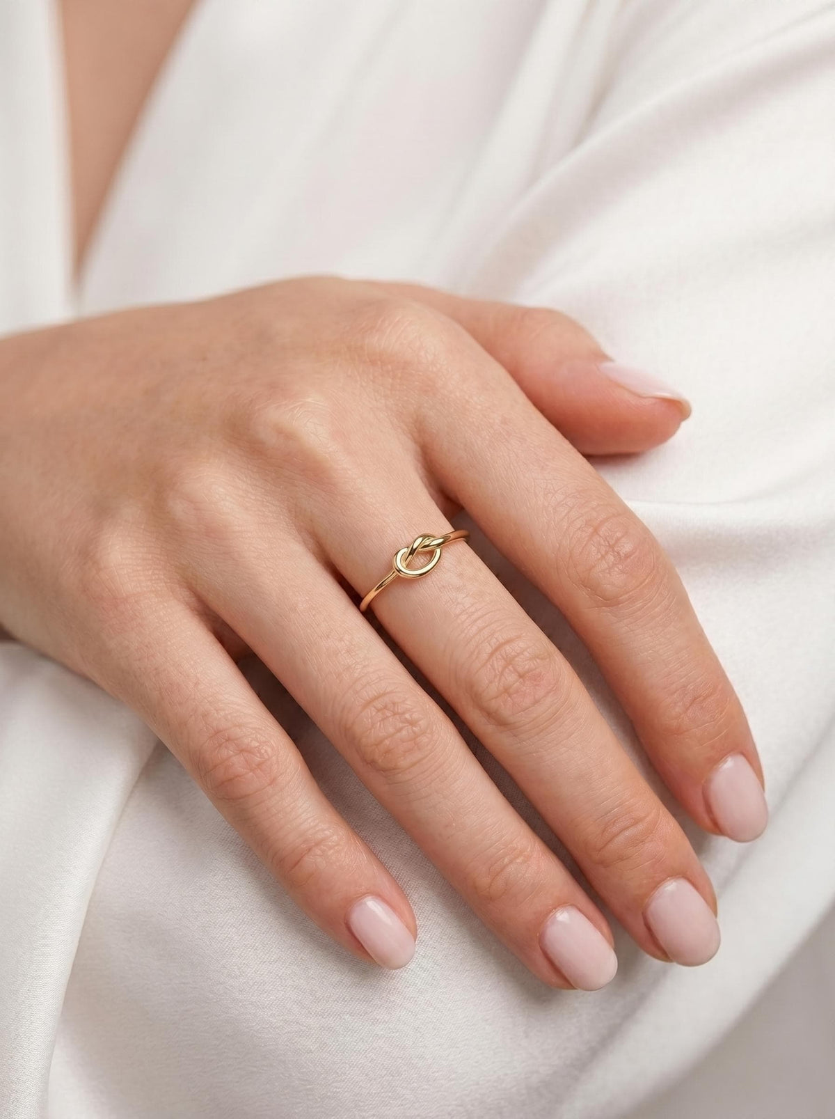Thin gold love knot ring stacked on the finger