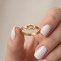 Solid gold lovers knot ring held between fingers