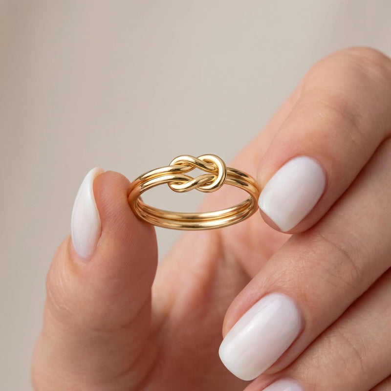Solid gold lovers knot ring held between fingers