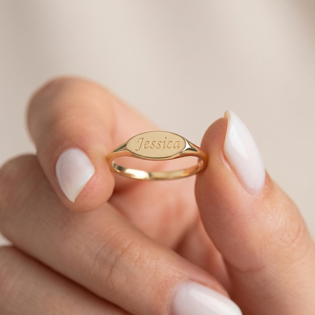 Oval signet ring engraved with a name, held in hand